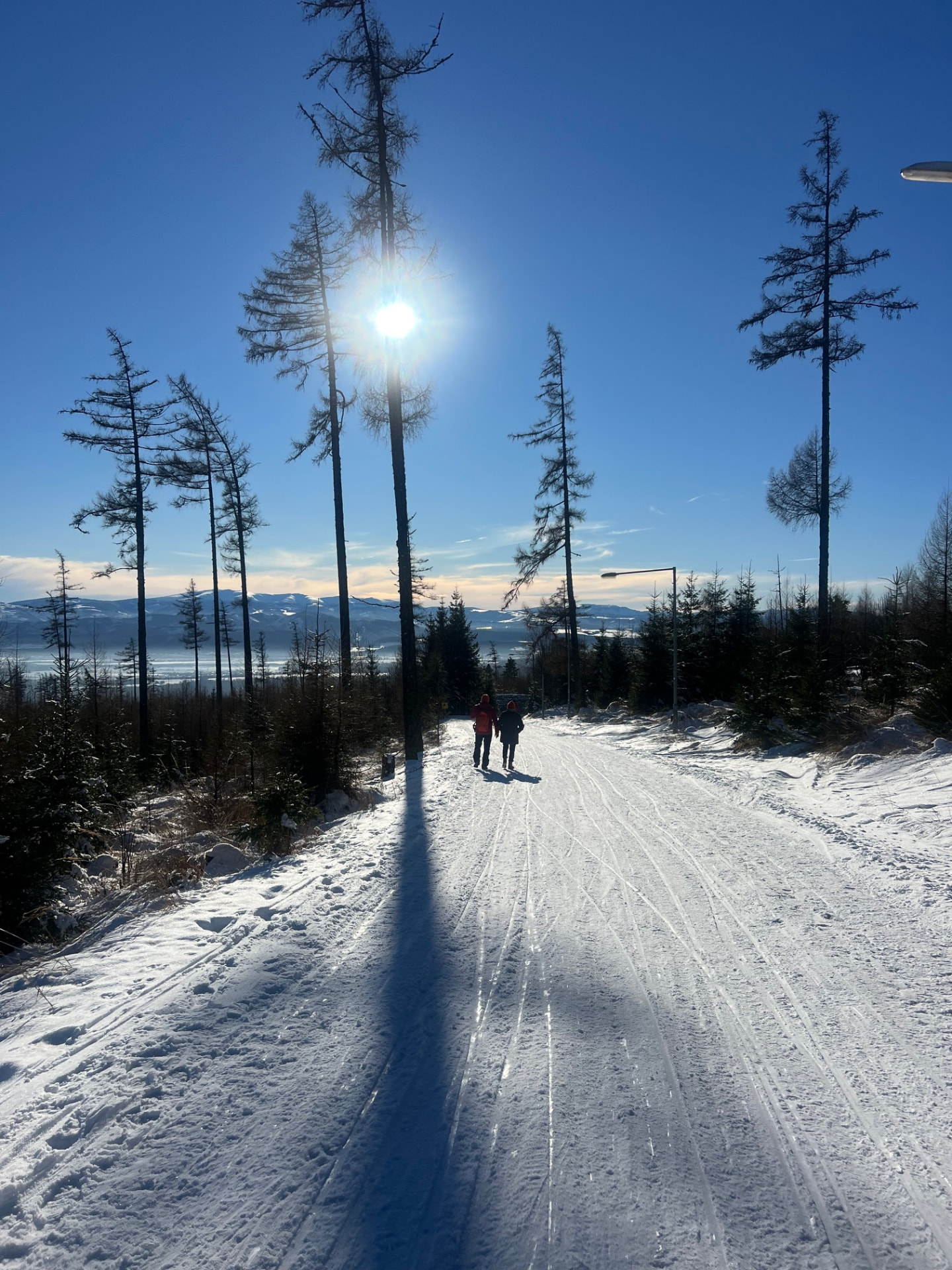Two people walking along a sunlit snowy mountain path in the High Tatras