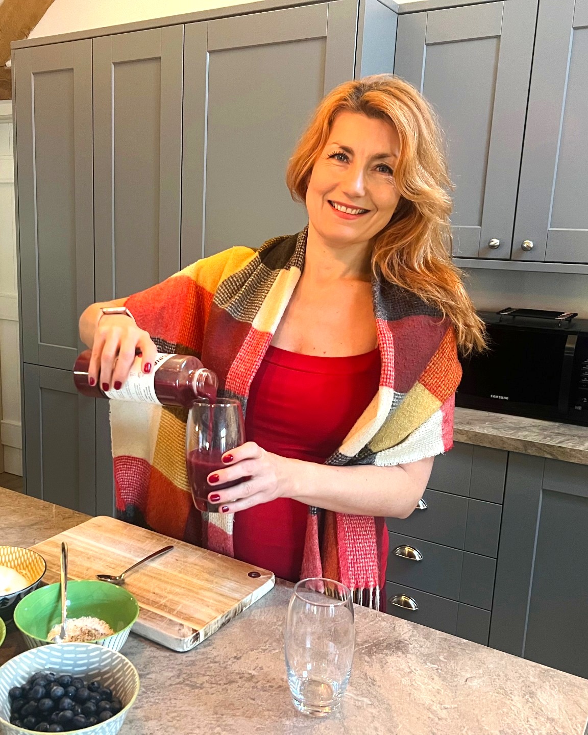 Julia pouring a berry smoothie in her kitchen, surrounded by fresh fruit and whole-food ingredients
