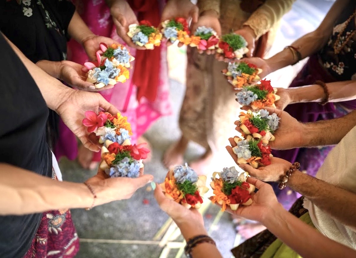 A circle of hands holding Balinese flower offerings out to one another
