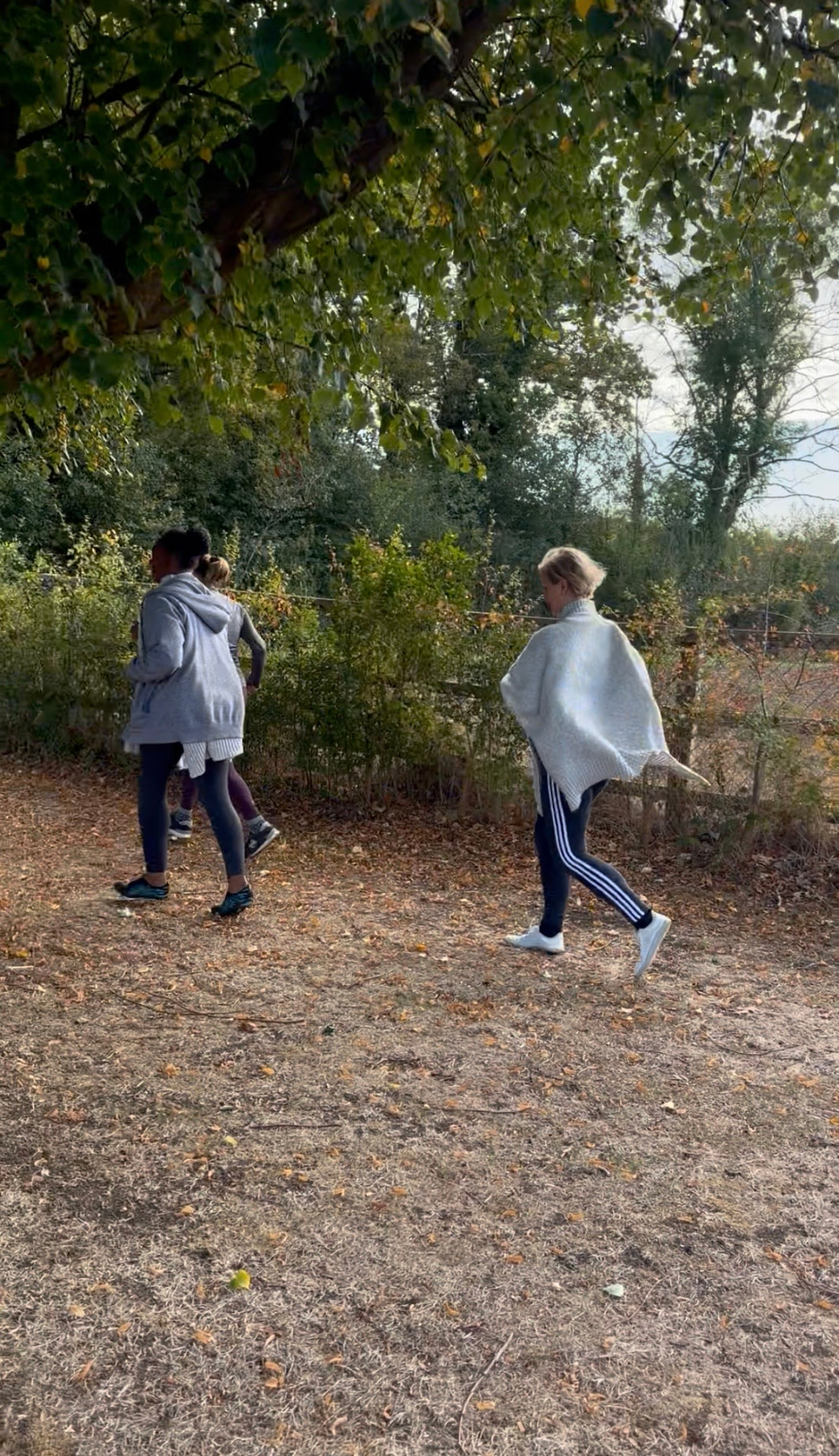 Three women walking together along a leaf-strewn autumn path