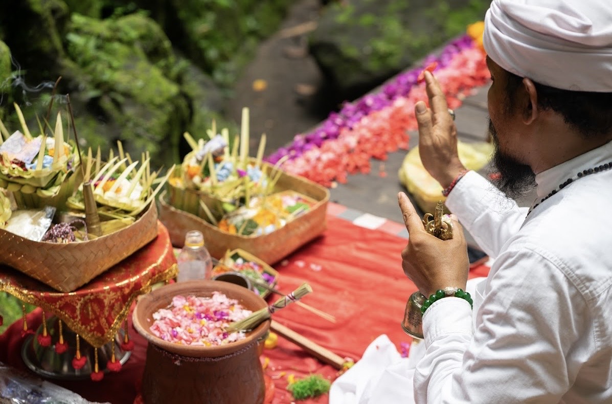 A Balinese priest offering flower blessings and incense during a river ceremony