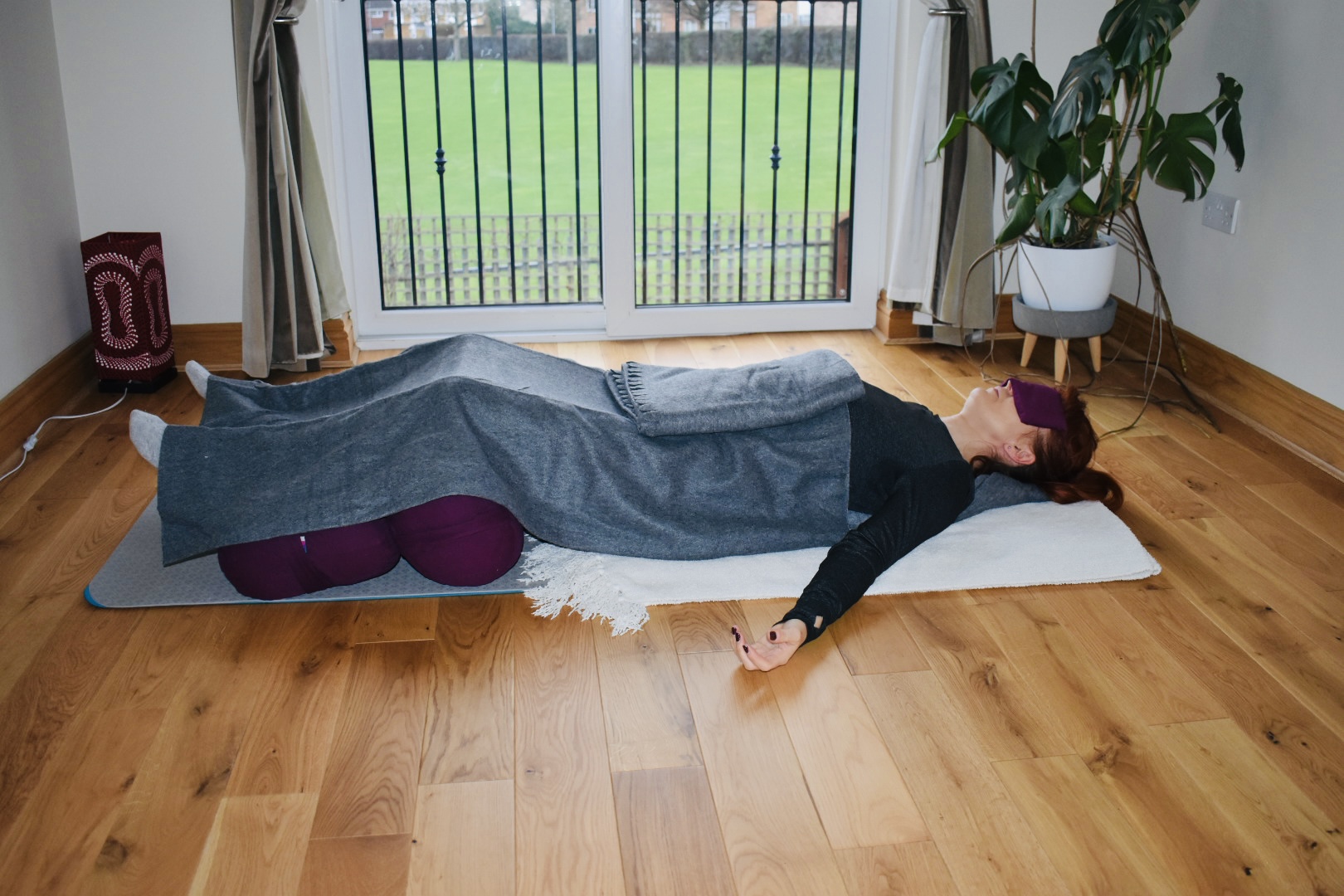 A fully supported restorative pose with bolster, blanket and eye pillow