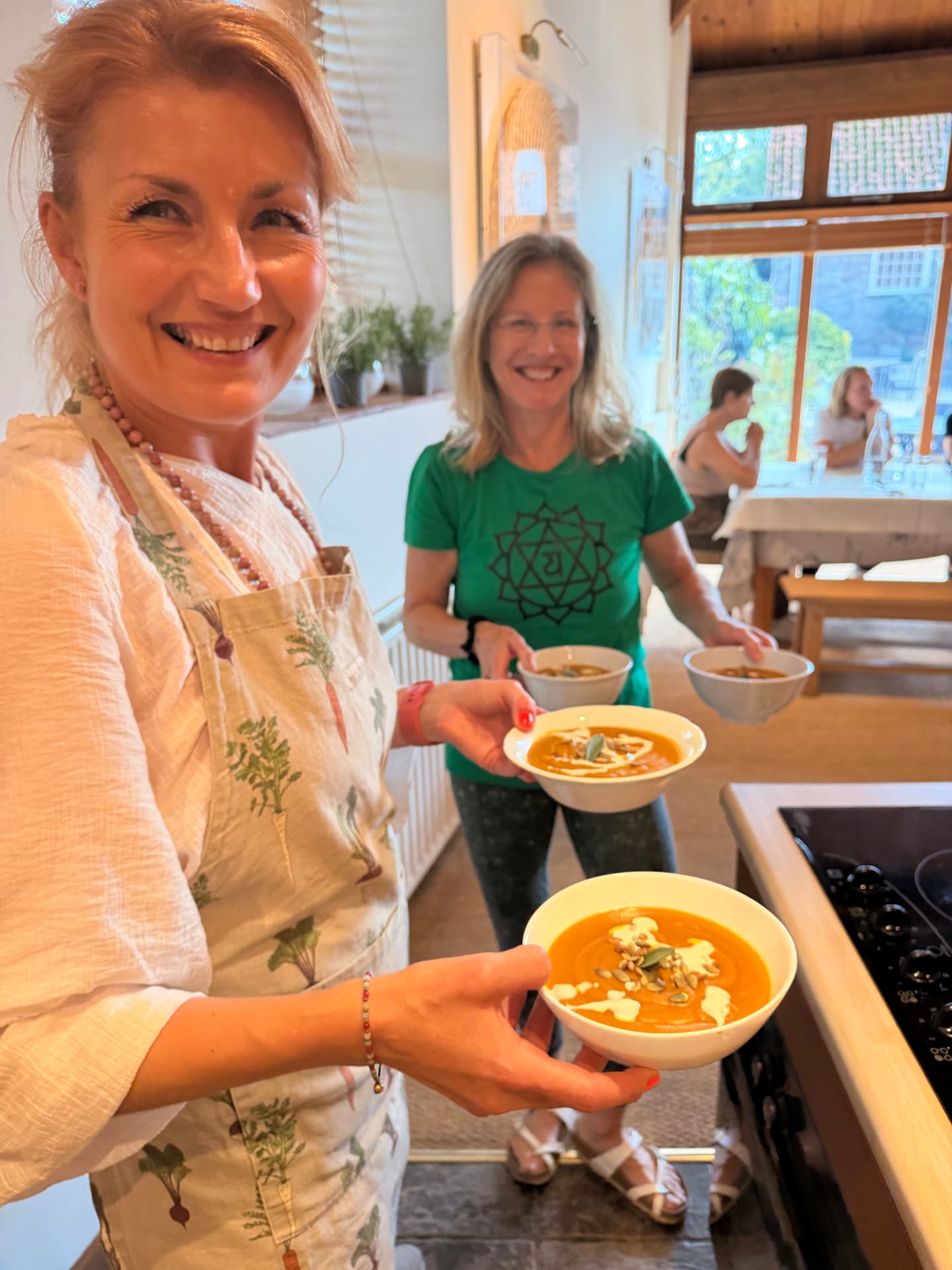 Julia smiling and serving bowls of roasted squash soup with a retreat guest in the kitchen at Tofte Manor