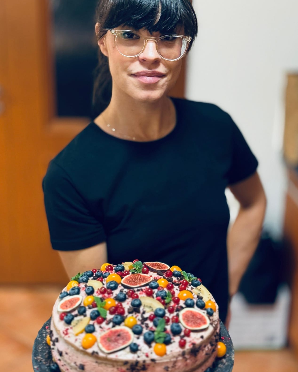 Chef Milica Fisher holding a handmade cake topped with figs, blueberries, redcurrants and physalis